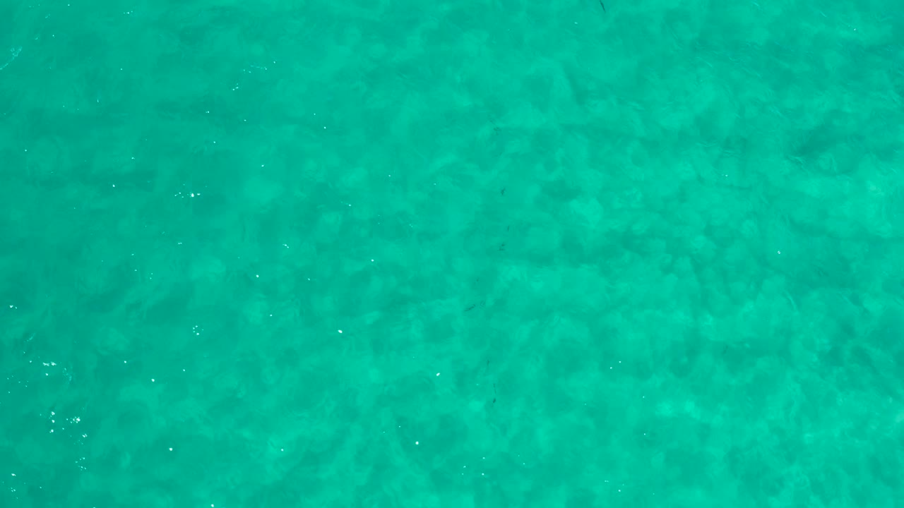 Clear aquamarine ocean surface in Los Cabos shows darker underwater patches beneath gentle ripples, with no visible people or vessels.
