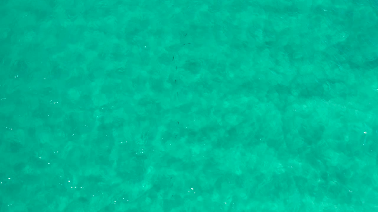 Turquoise ocean surface in Los Cabos, Mexico, with darker submerged areas across the frame and no visible people.