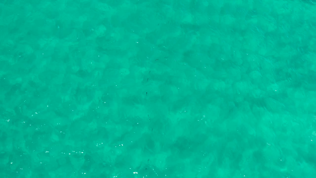 Aqua ocean water fills the frame in Los Cabos, Mexico, with soft ripples and scattered white glints, no visible people.