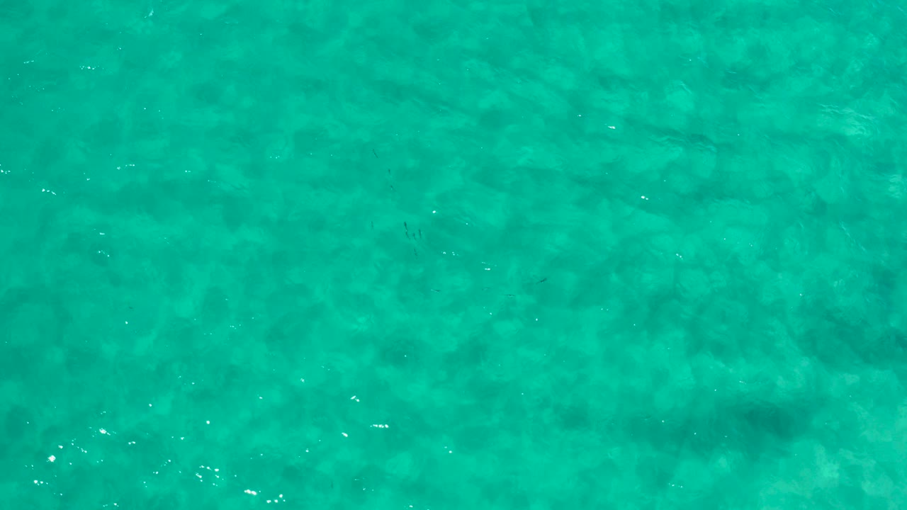 Opening frame of turquoise shallow ocean water in Los Cabos, Mexico, with faint submerged rock or sand patterns and no visible people.