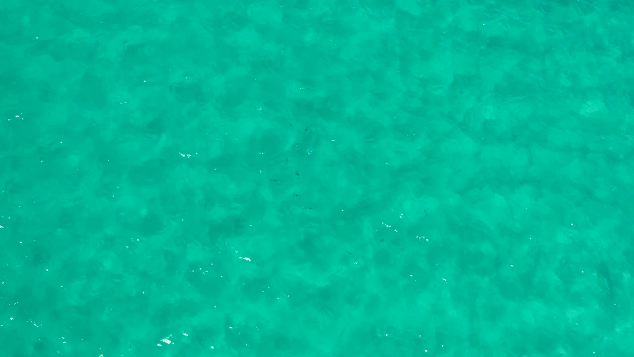 Top-down view of turquoise sea in Los Cabos, Mexico, with faint darker underwater patches and no visible people.
