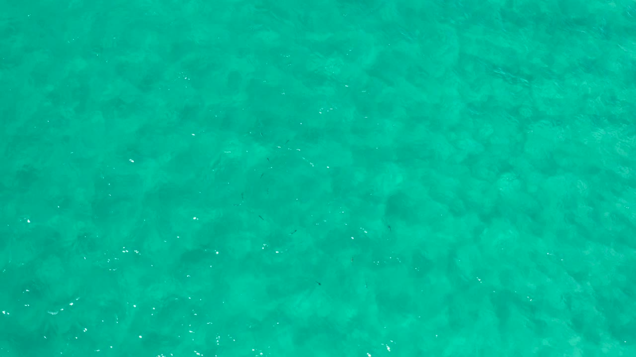Turquoise shallow water with faint seabed texture and small sun glints.