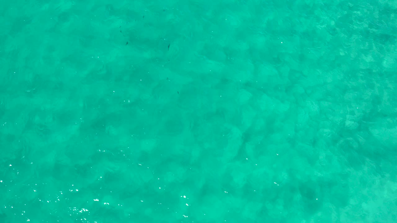 Top-down aerial view of turquoise water in Los Cabos, Mexico, with faint darker underwater patches and no visible people.