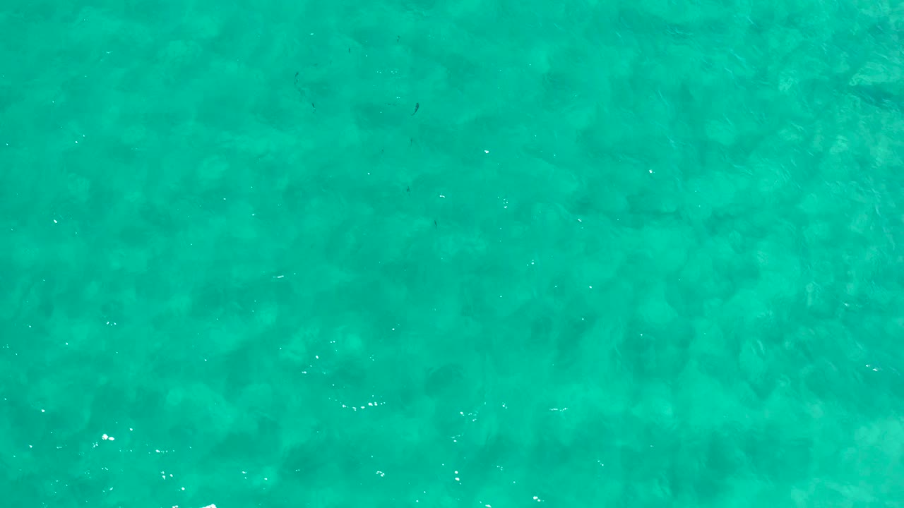 Overhead turquoise water in Los Cabos, Mexico, shows mild ripple highlights and mottled darker areas beneath the surface, with no visible people.
