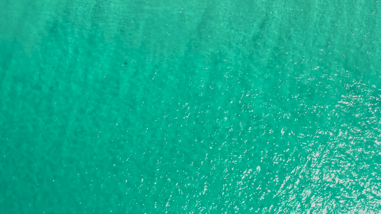 Straight-down frame of turquoise Los Cabos ocean water with even ripple patterns, a pale highlight patch near the lower middle, and no visible people.