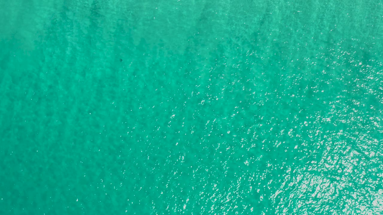 Overhead aqua sea in Los Cabos, Mexico, with scattered silver reflections across the left and center and no boats, shore, or visible people.
