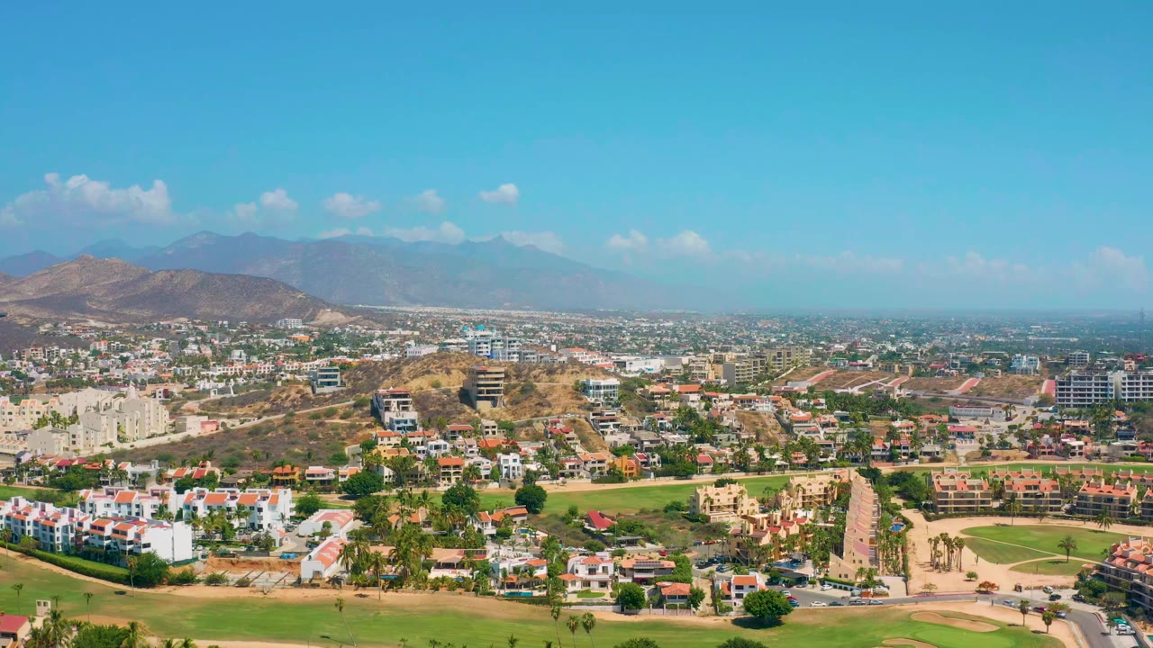 Aerial townscape with residential blocks, roads, dry hills, and mountains.