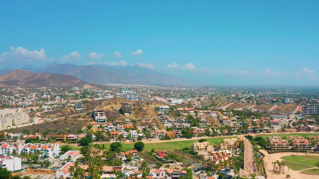 Third frame shows Los Cabos suburban homes and lawns in the foreground, denser buildings beyond, mountains on the horizon, scattered clouds, and no visible people.