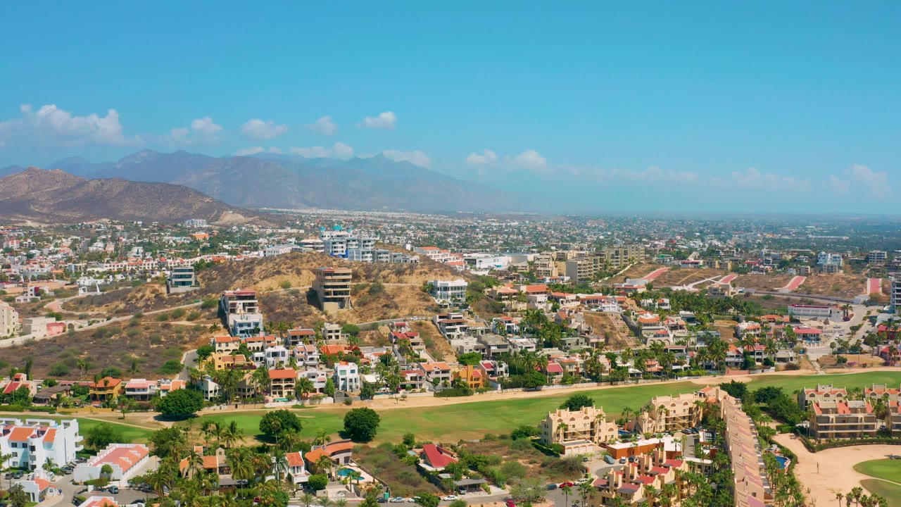 High aerial view of residential blocks, green grounds, hills, and mountains.