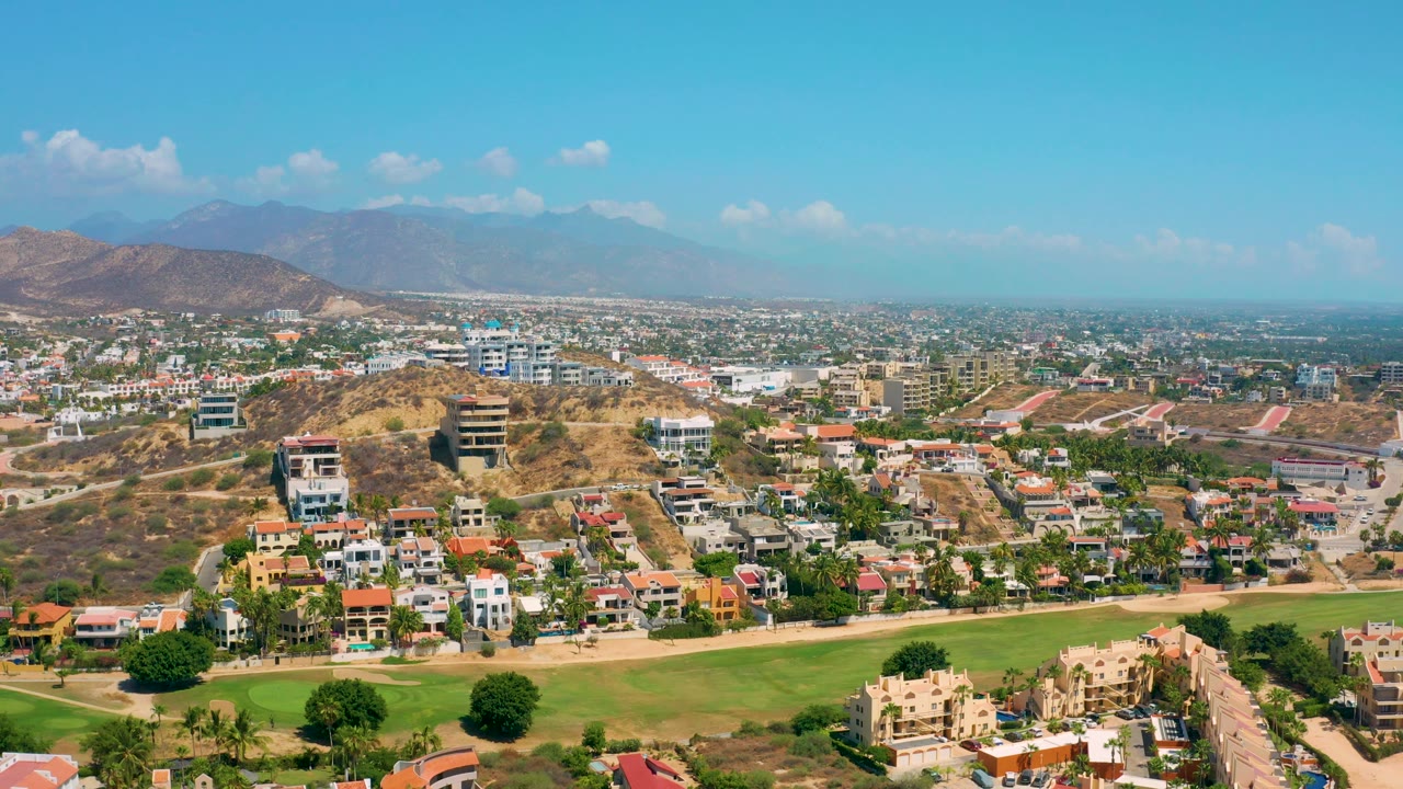 High view across hillside neighborhoods, open green grass, distant city, and blue sky.