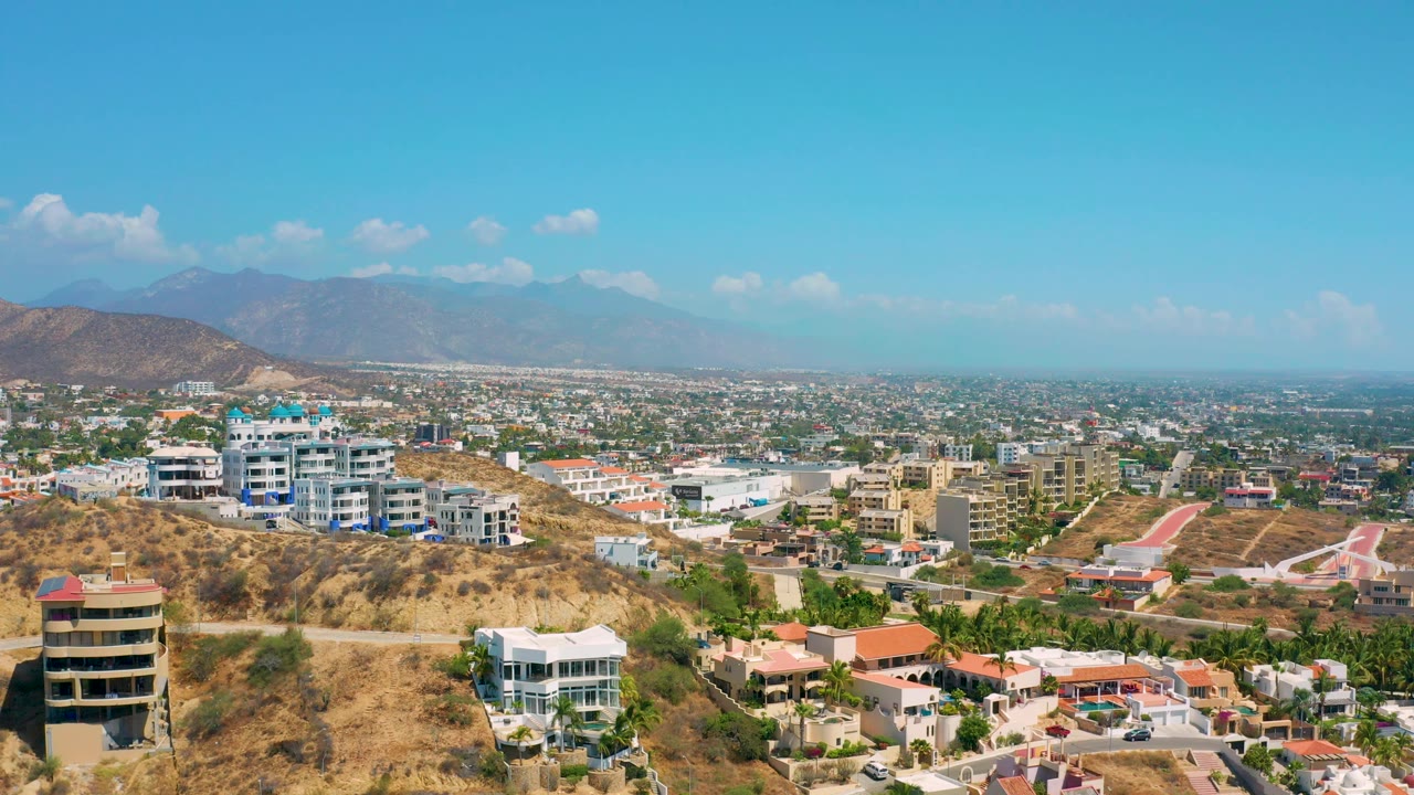 Hillside buildings overlook a low city grid with hazy mountains in the distance.