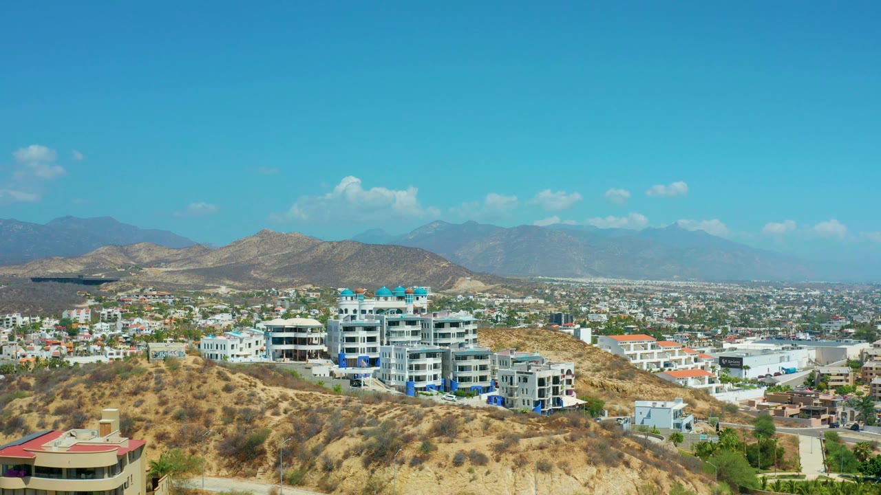 Dry hill foreground, resort buildings, cityscape, mountains, and blue sky.
