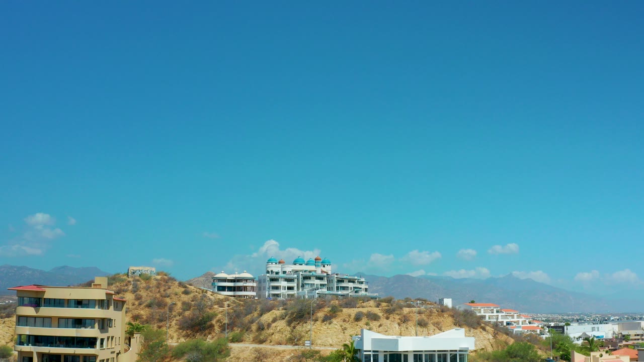 Hillside homes and apartment buildings under a wide blue sky.