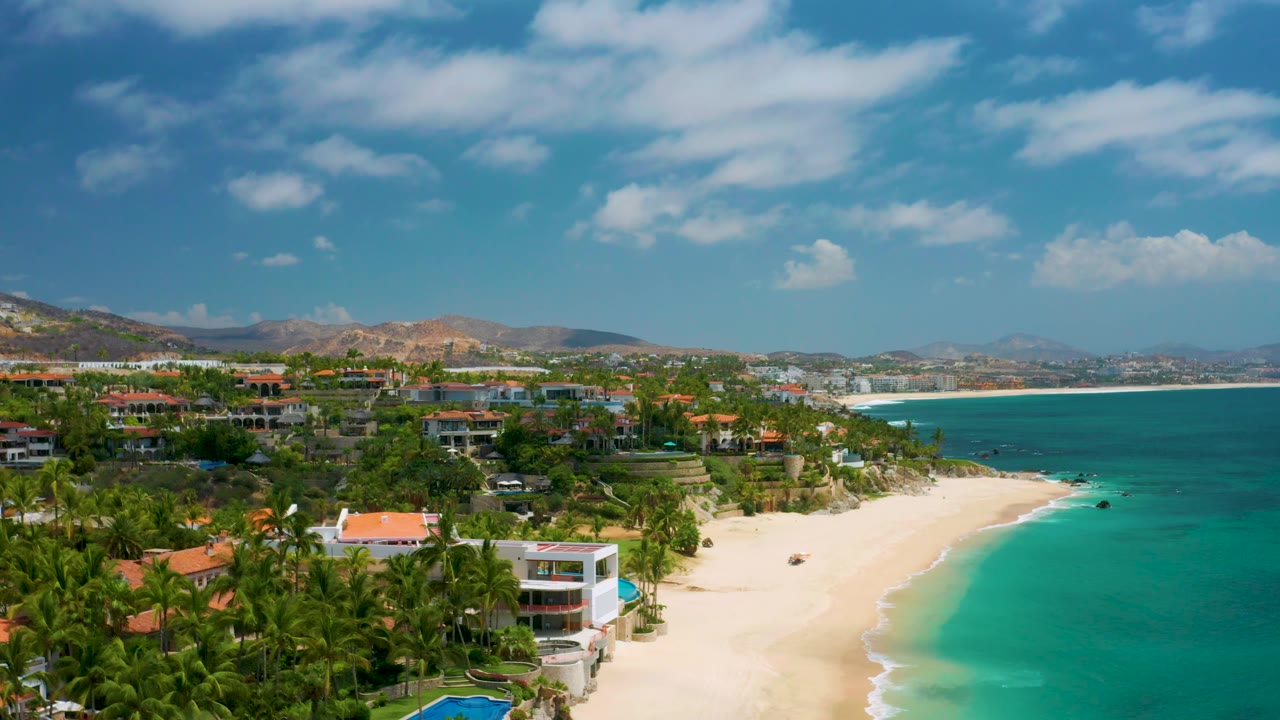 Aerial coastline view with resort greenery, sandy beach, and open blue water.