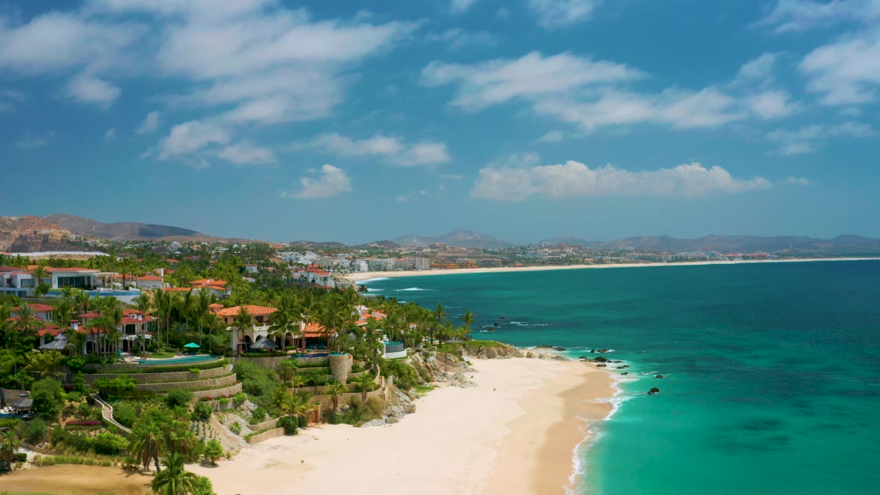 Aerial-style view of homes, beach, turquoise surf, and distant shoreline