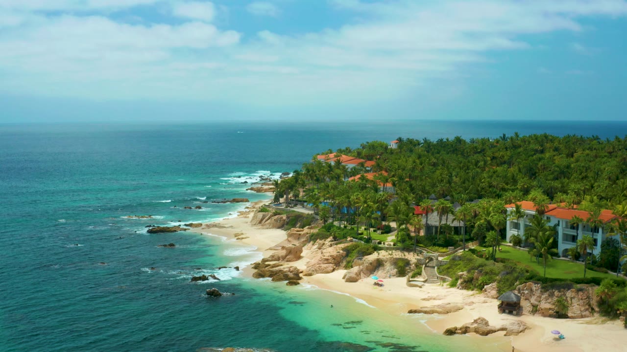 Aerial beach view with darker ocean foreground and homes along the palm-covered shore