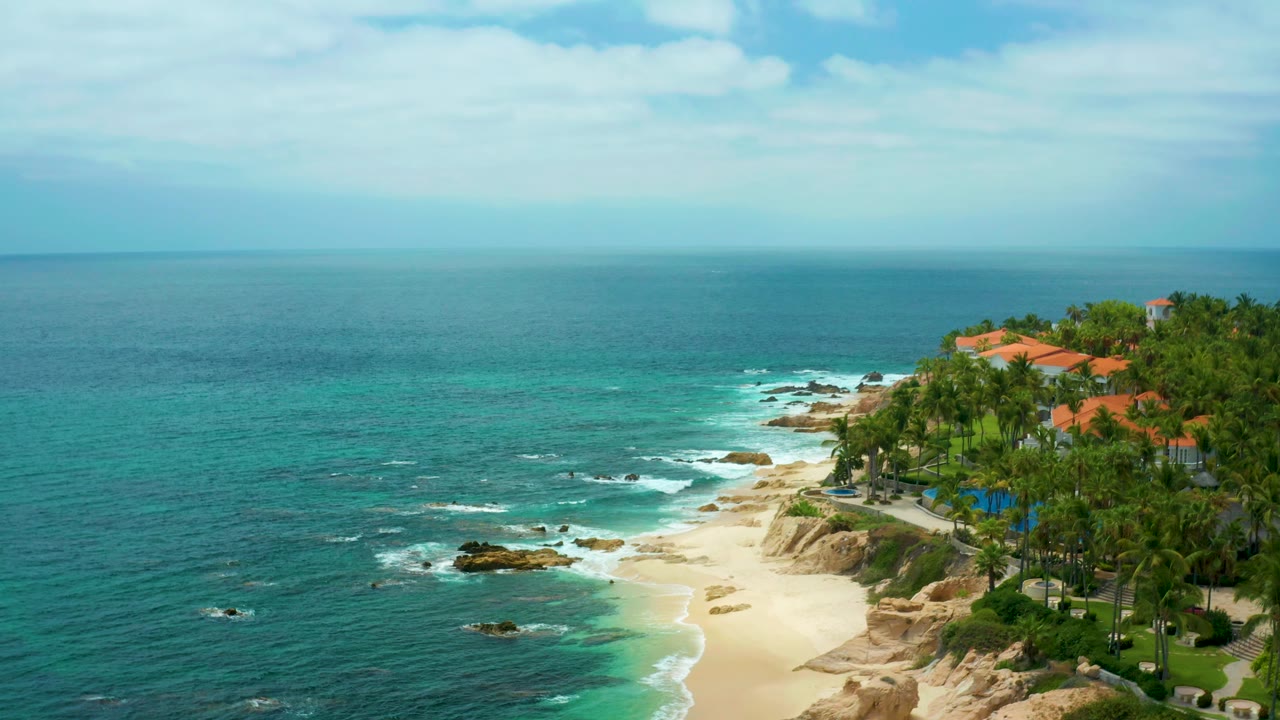 Elevated coastline view with beach, rocks, palms, lawns, and ocean horizon