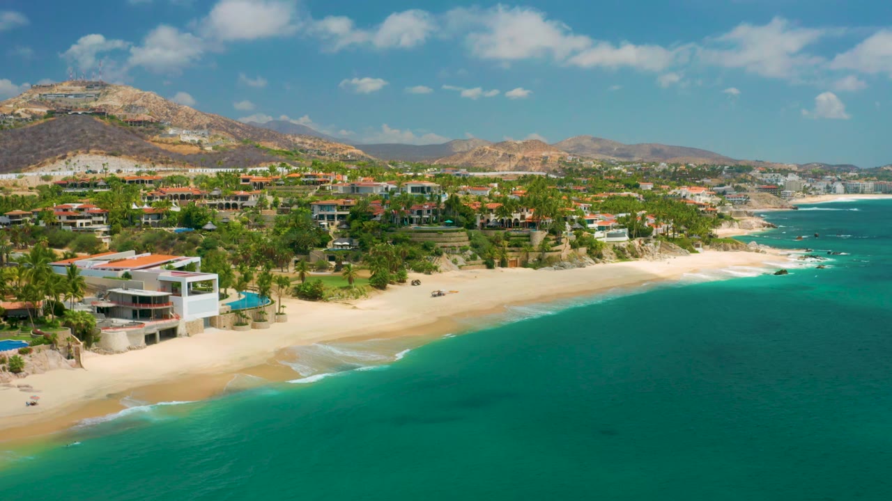 Coastal homes and palm trees above a sandy beach with turquoise water.
