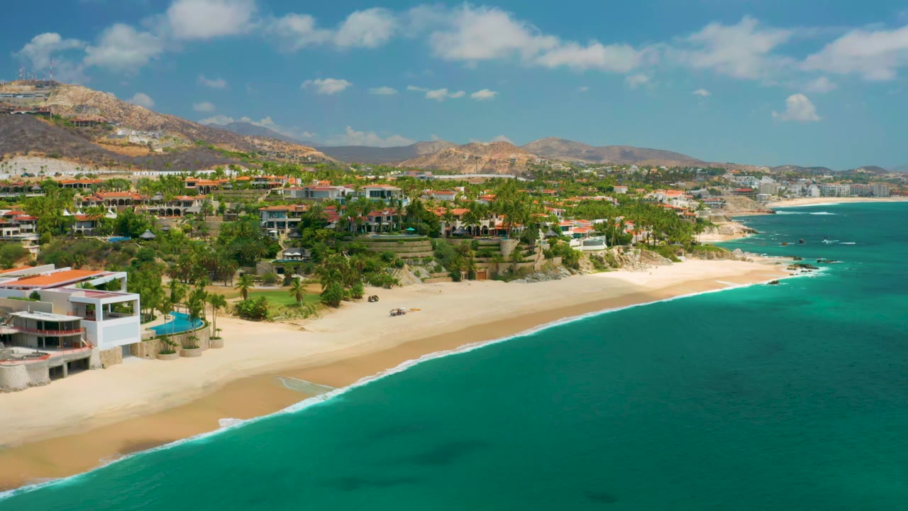 Wide aerial coastline with beach homes, palms, mountains, and blue water