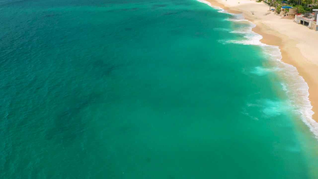Turquoise sea and surf line beside a sandy beach with buildings above.
