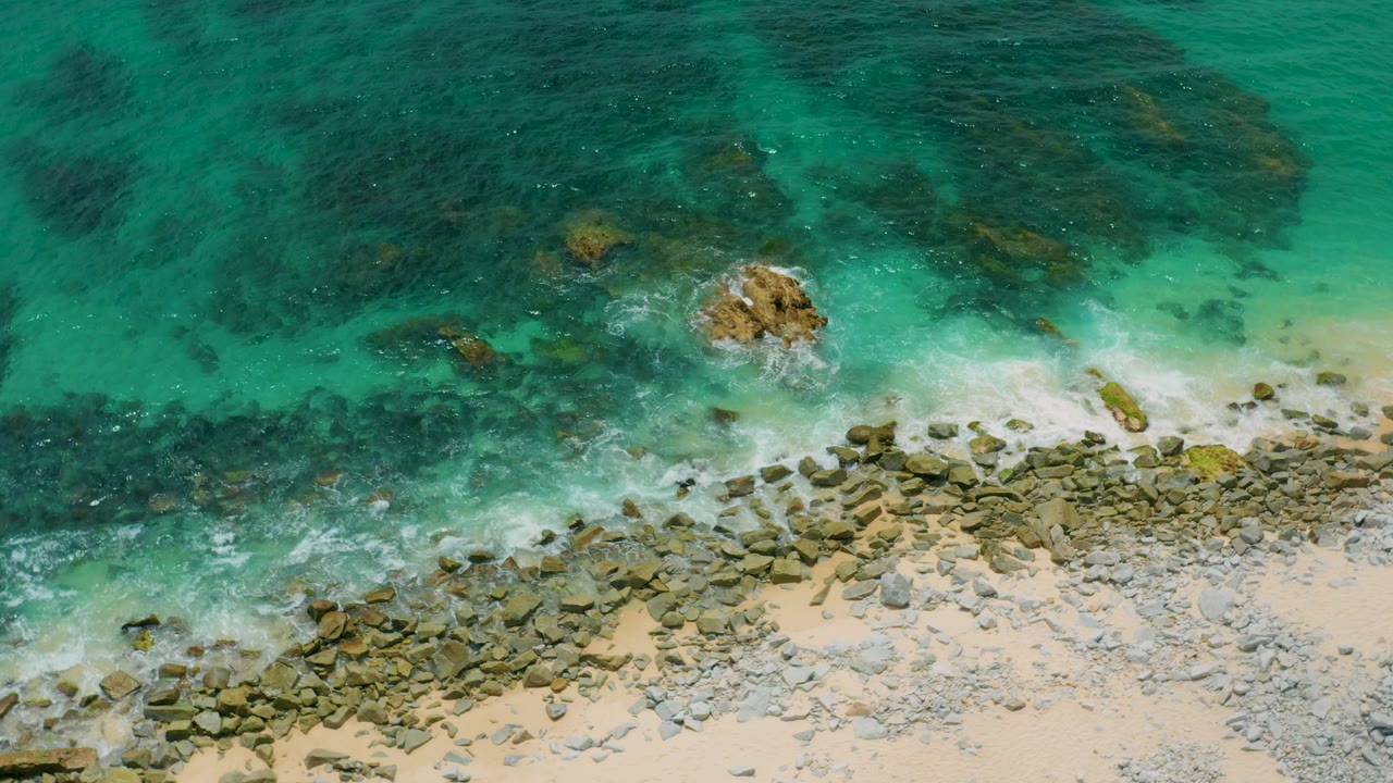 Top-down beach water with foam curling around a central rock.