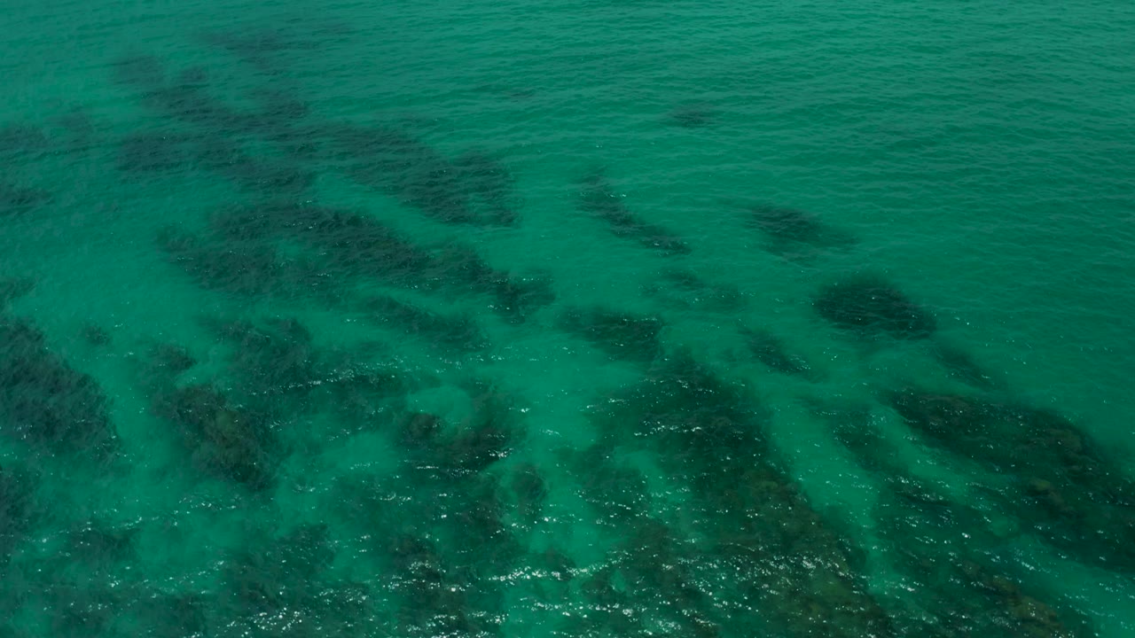 Overhead Palmilla Beach Cabo water frame with soft wave shadows crossing dark seabed patches and open turquoise water, no visible people.