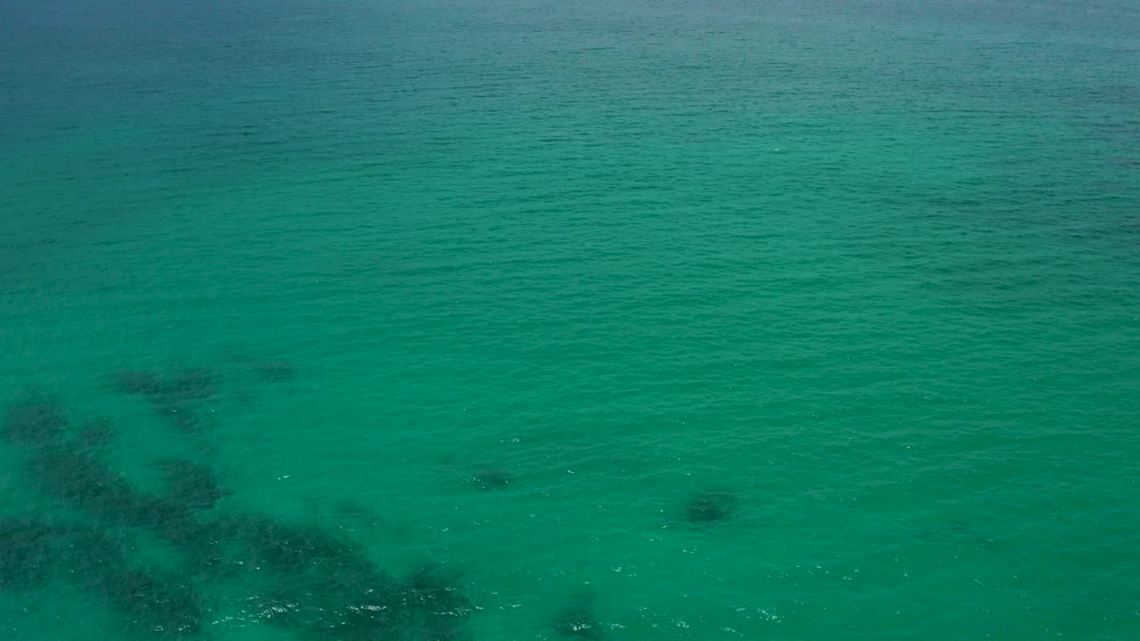 Aerial view of green-blue ocean water at Palmilla Beach Cabo, Mexico with dark underwater patches near the lower left and no visible people.