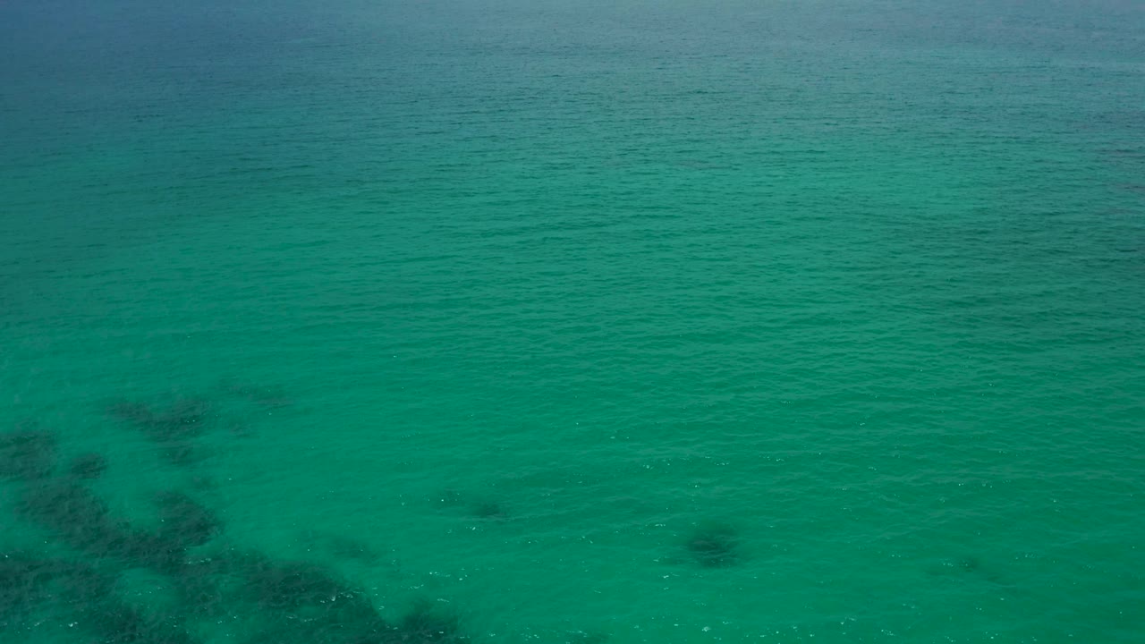 Turquoise ocean at Palmilla Beach Cabo, Mexico with a larger dark submerged cluster toward the lower half of the frame and no visible people.