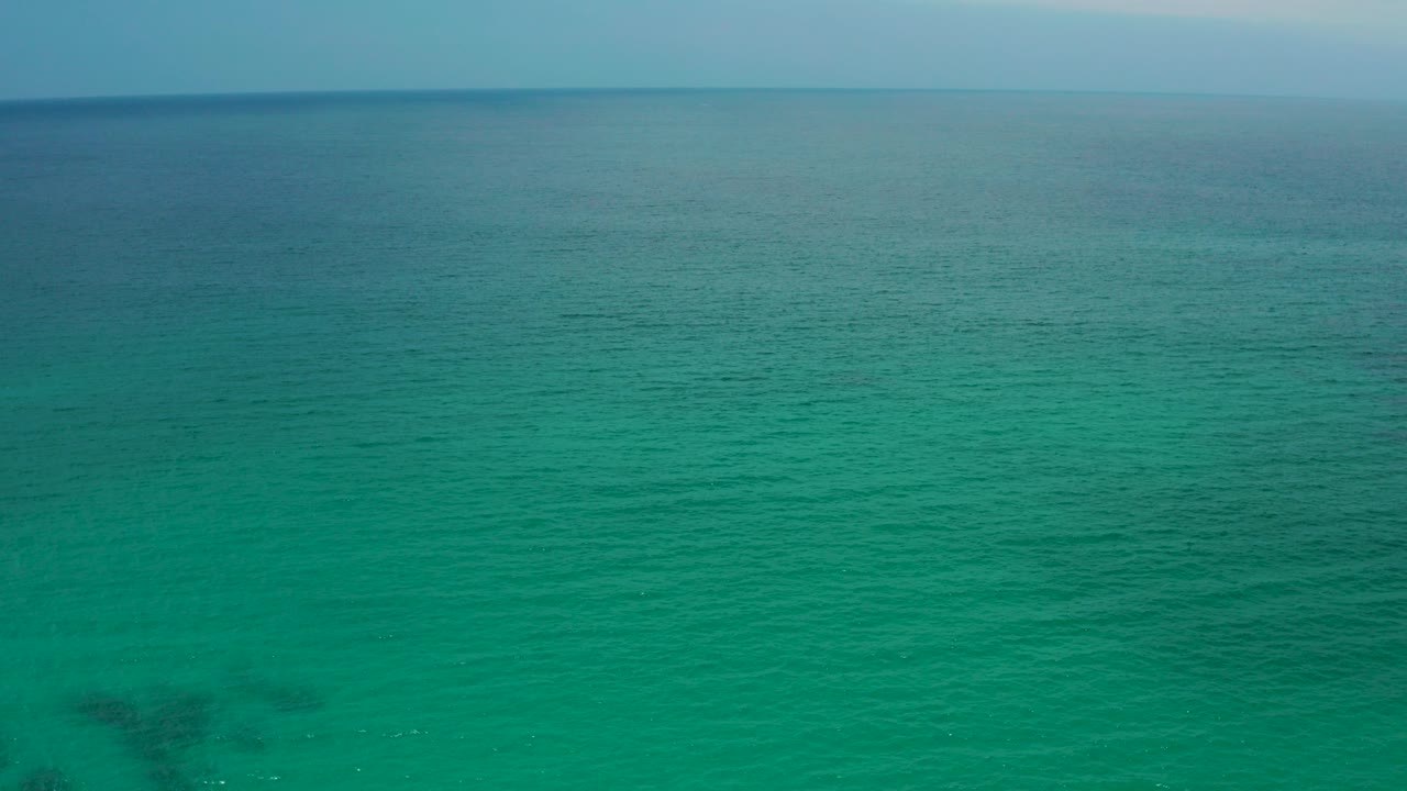 Opening frame of turquoise-green ocean at Palmilla Beach Cabo, Mexico, with a distant straight horizon, faint underwater dark patches, and no visible people.