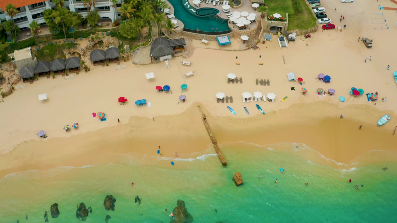 Aerial view of beach umbrellas, lounge chairs, palapas, and shallow water.