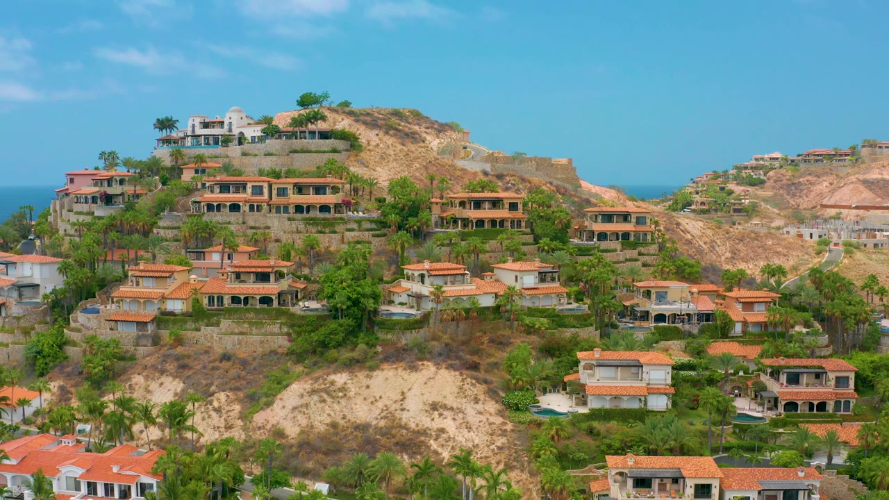 Hillside neighborhood with villas, cliffs, palms, and blue sky.