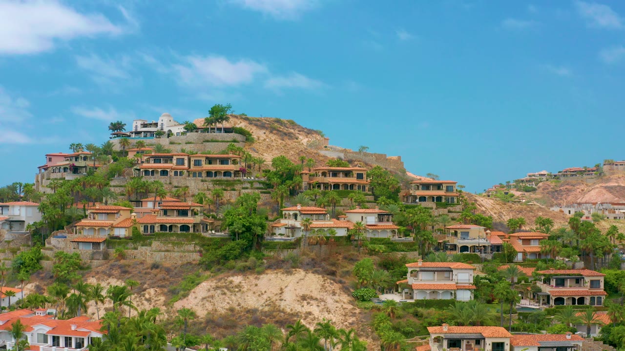 Wide hillside view with houses, trees, and bright sky.