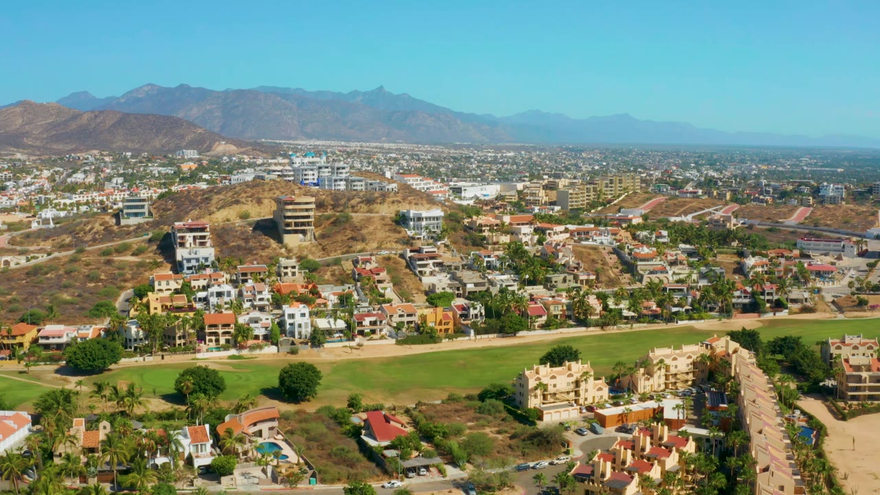 Wide aerial over houses, hillside lots, town buildings, and mountains.