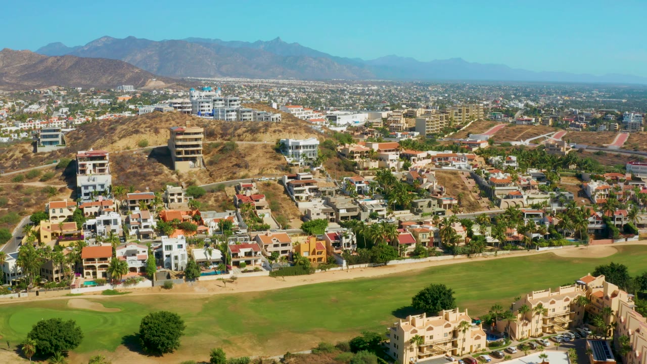 Aerial view of hillside neighborhood, green lawn, roads, and distant mountains.