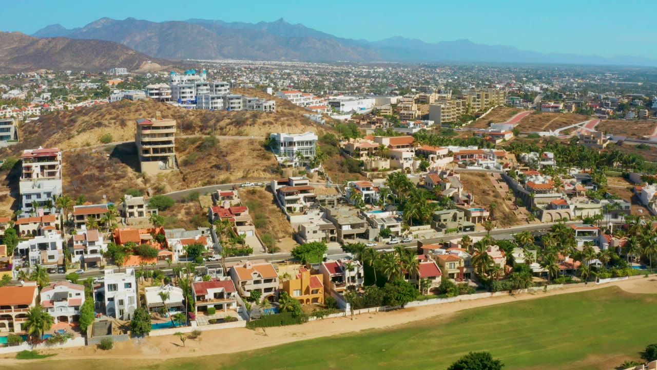 Aerial neighborhood view with field, homes, and dry hills.