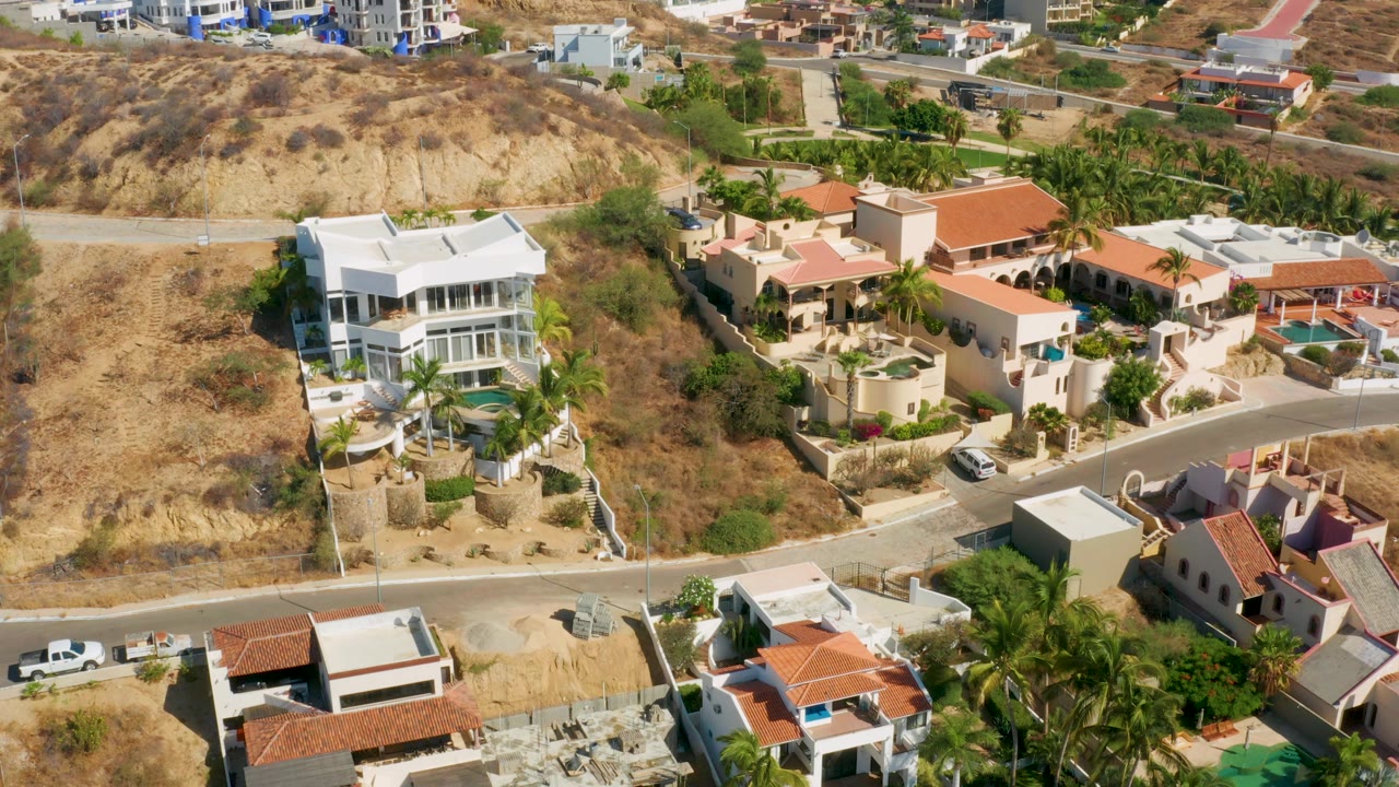 San Jose del Cabo aerial frame showing clustered residential properties, a curved road, palms, tan scrubland, and no visible people.