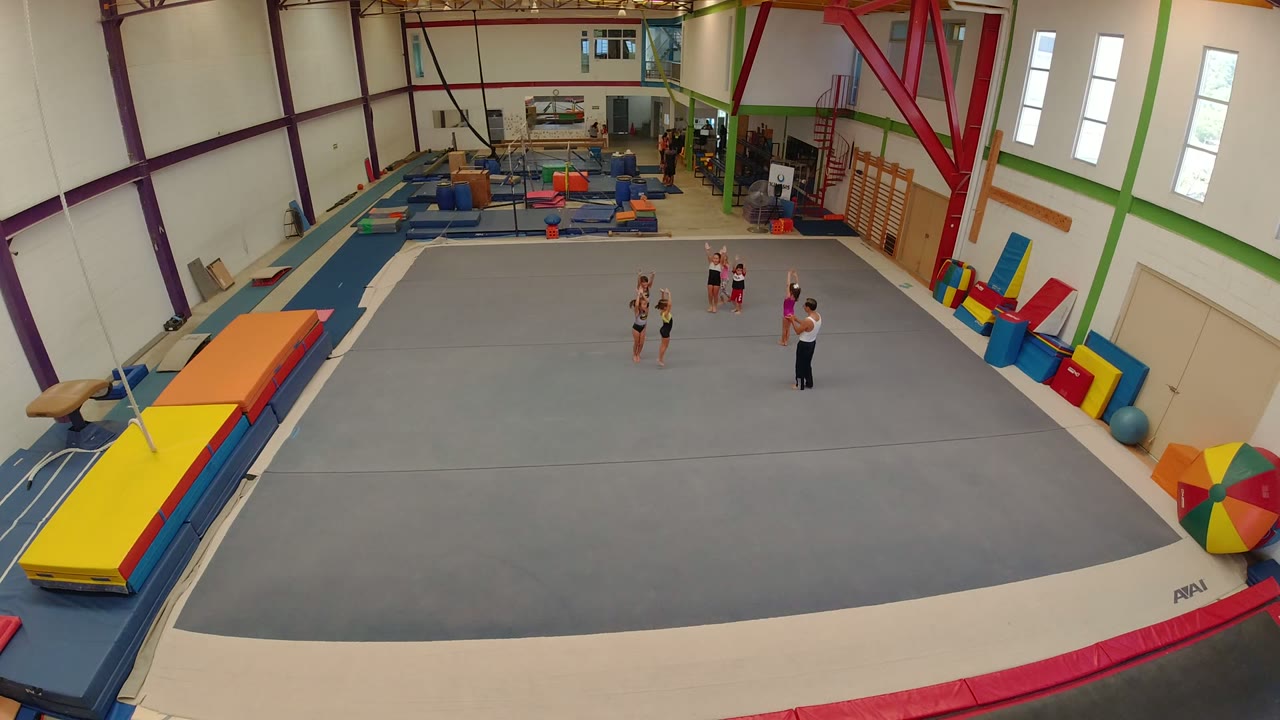 Children cluster closer to an adult on the gray floor in the Los Cabos indoor gym, with colorful mats and training equipment lining the walls.