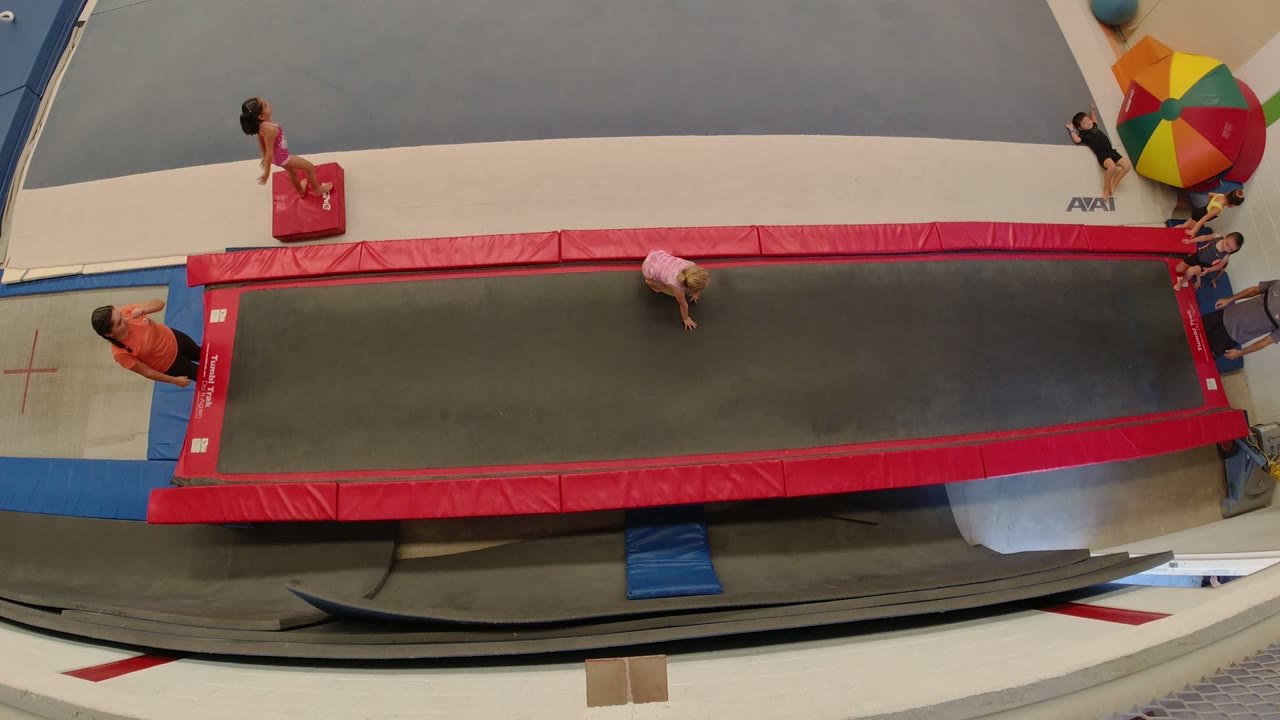 Overhead view of a red trampoline with children and a coach nearby.