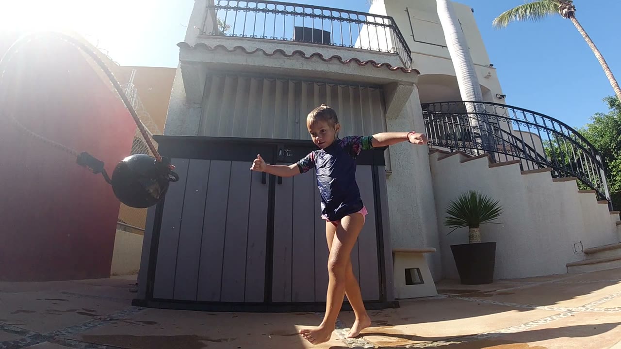 Young girl balancing near a black ball on a sunny pool deck.