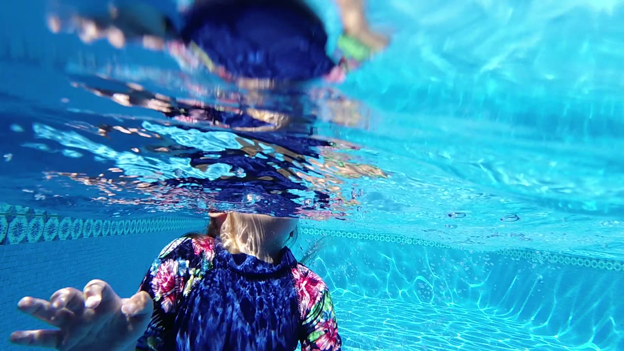 Swimmer partly underwater in a blue pool with a hand reaching forward.