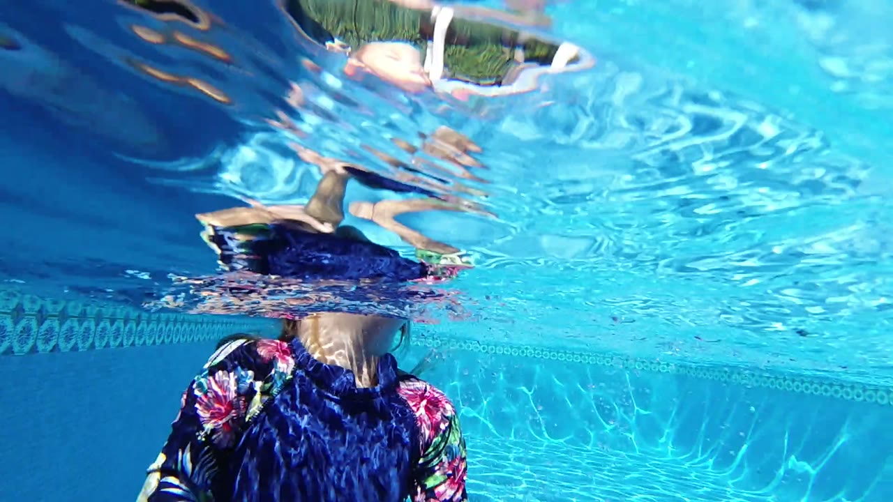 In Los Cabos, Mexico, the swimmer is centered beneath the shimmering pool surface while distorted reflections of arms and legs appear along the top of the frame.