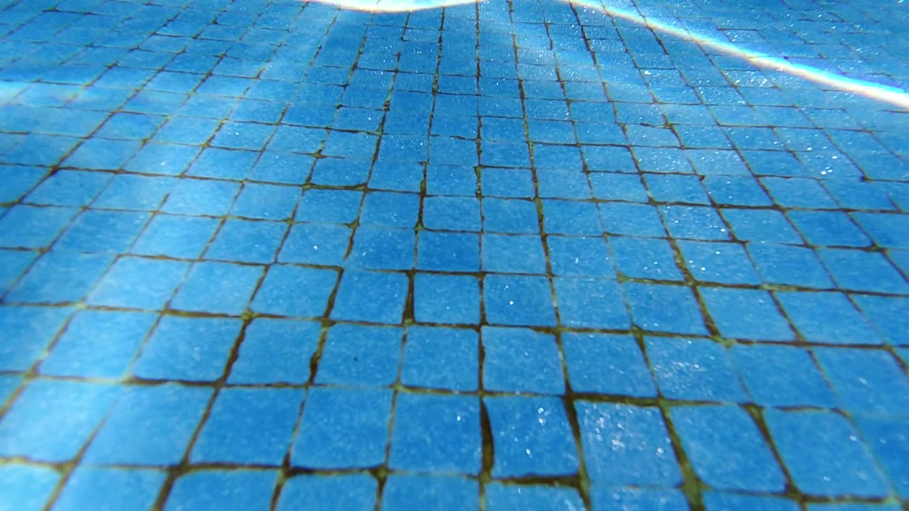 Blue underwater pool tiles with bright reflected sunlight.