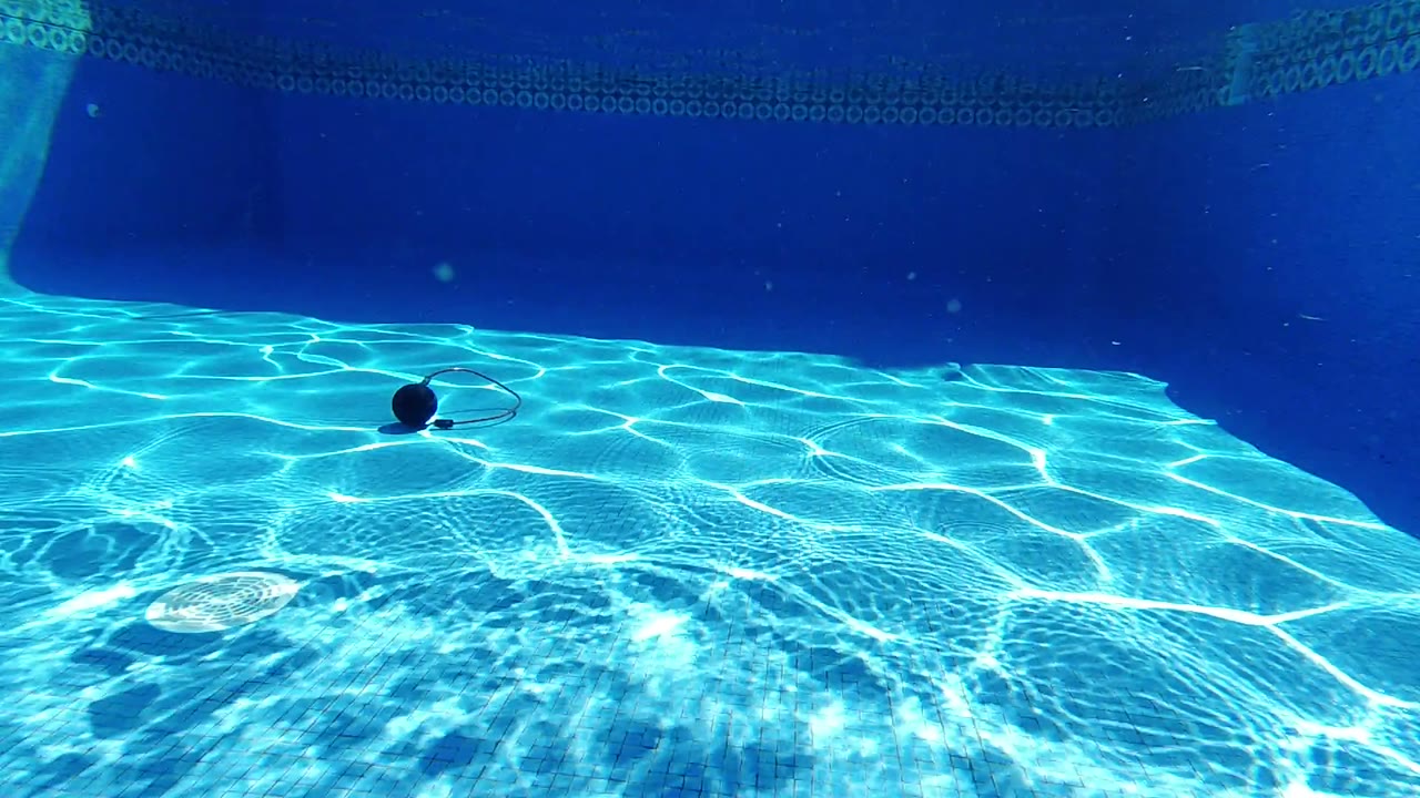 One second into the Los Cabos clip, the dark round object sits slightly left of center on the pool floor as bright turquoise reflections spread across the water, with no visible people.