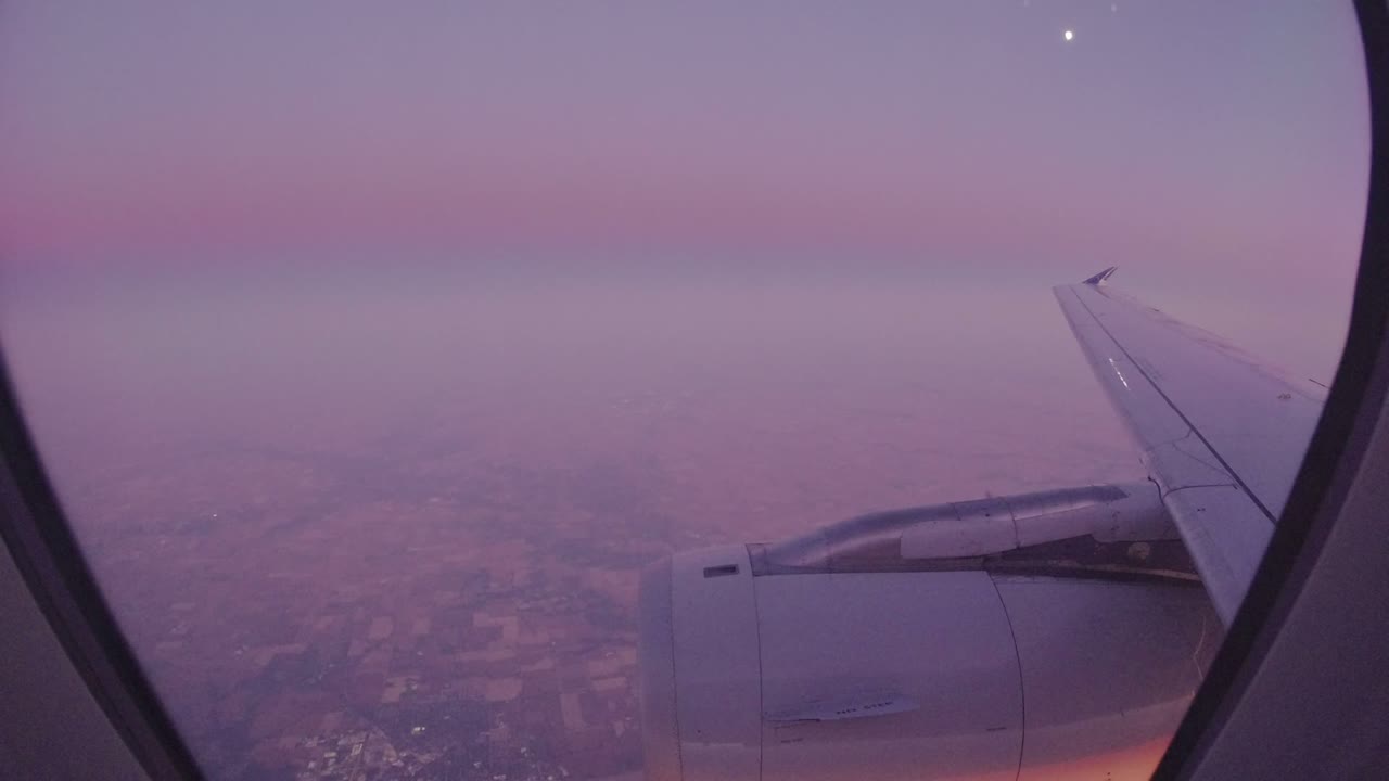 Airplane wing and engine seen through a passenger window above hazy land.