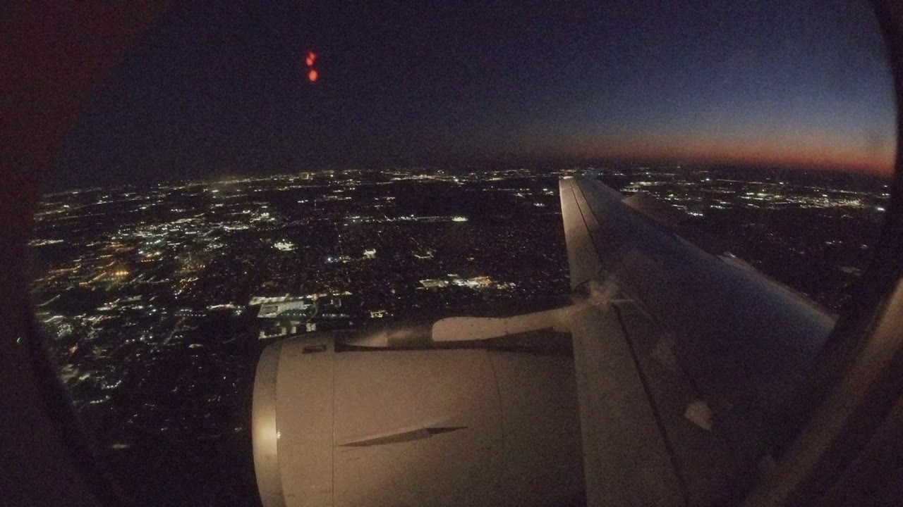 Airplane wing and engine over city lights at night.