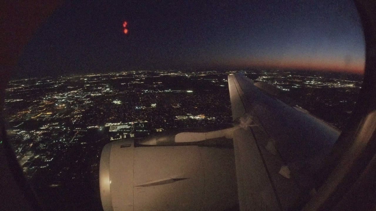 Airplane window frame at night over Los Cabos, Mexico, with the engine low in frame, the wing angled right, scattered city lights below, and no visible people.