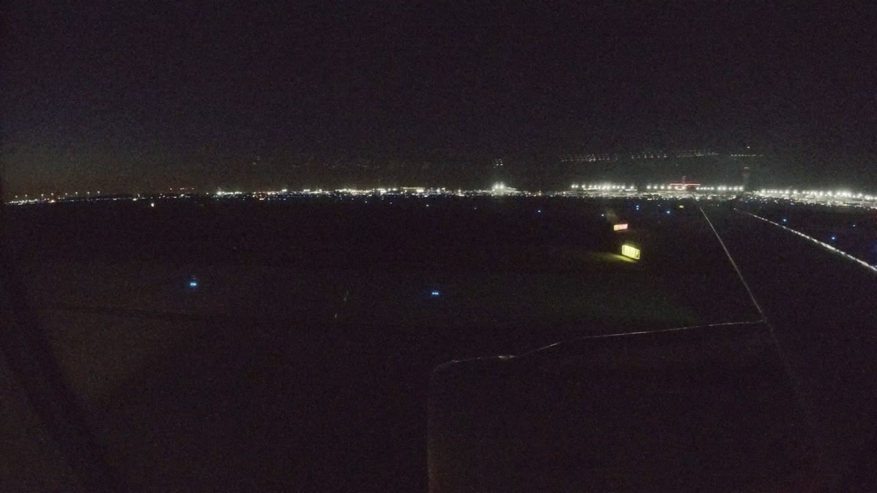 Los Cabos nighttime landing view with the aircraft wing darker in the foreground, a diagonal line of runway lights, distant airport illumination, and no visible people.