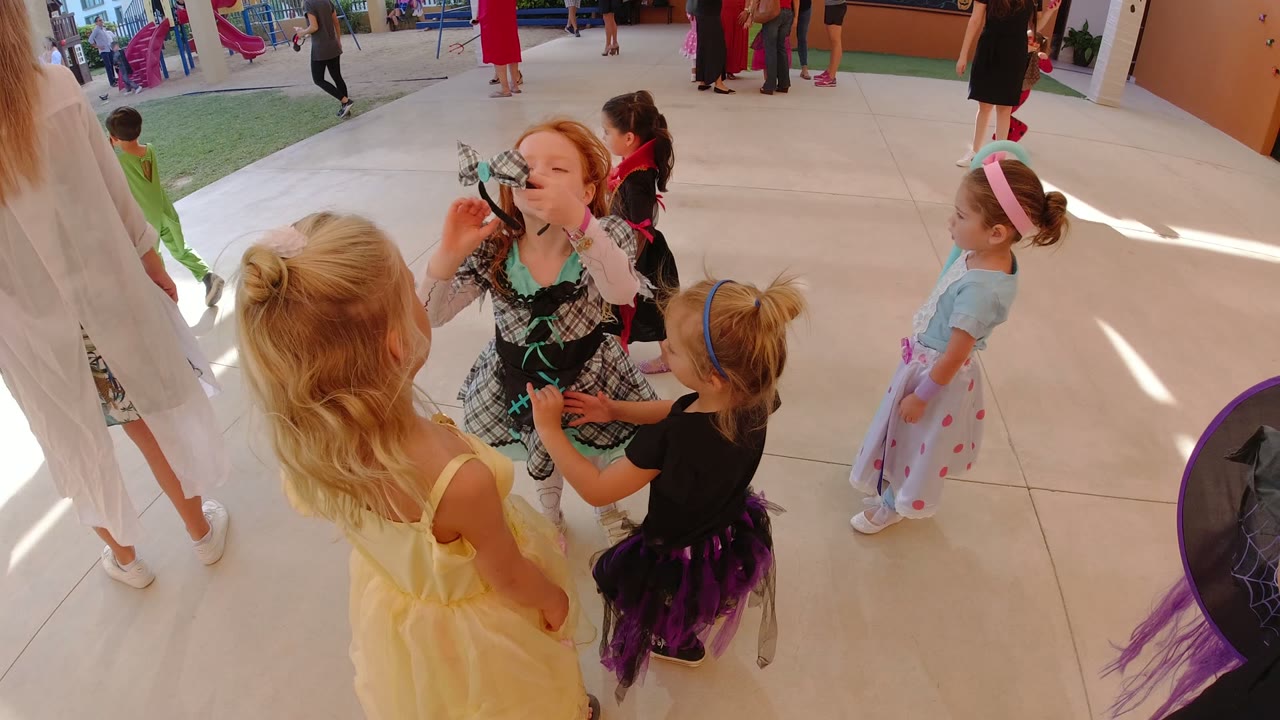 A girl in a plaid fancy dress costume raises her face near two other children in dress-up clothes during the Los Cabos outdoor school party.