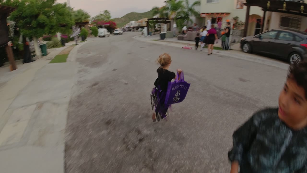 Child with a purple bag crossing a residential street as another child passes close to camera.