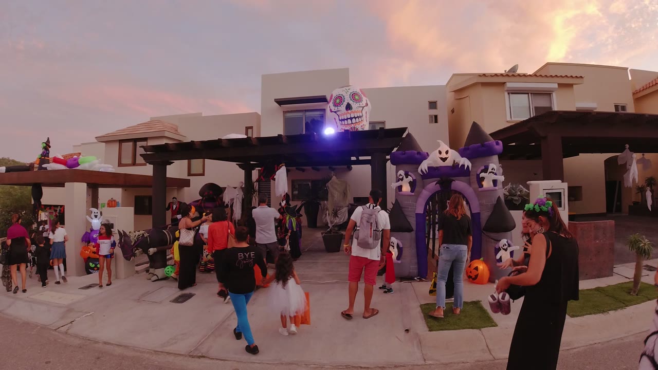 Families in costumes gather outside a decorated Halloween house at sunset.